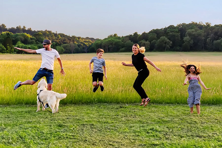 Sam & Matt with their children jumping in a field as a family.