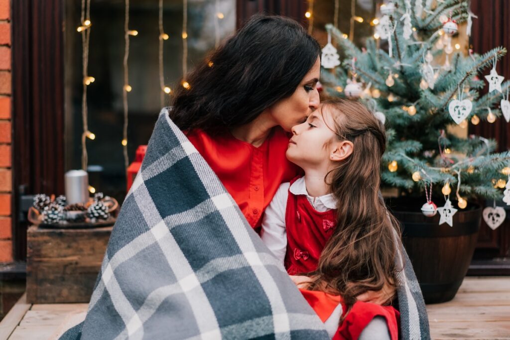 Mother hugging and wrapping her daughter in a blanket during the Festive Season.